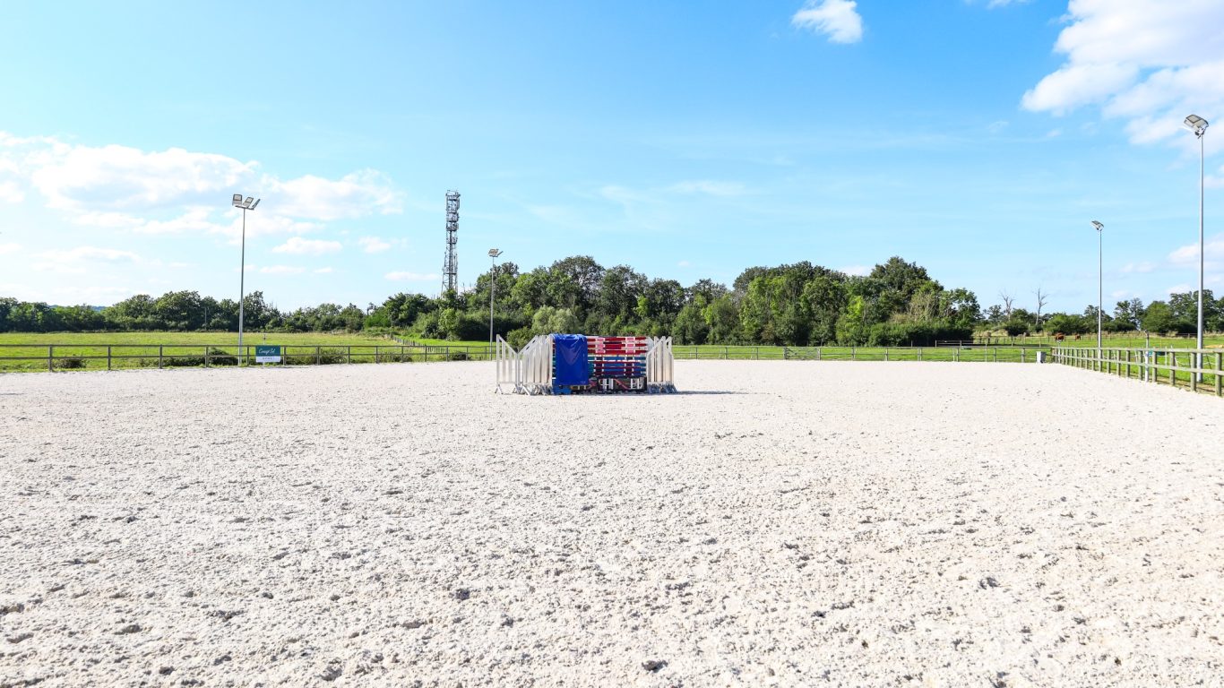 Carrière de 50m x 80m Réserve équestre avec une surface de sable, clôturée et équipée de panneaux.