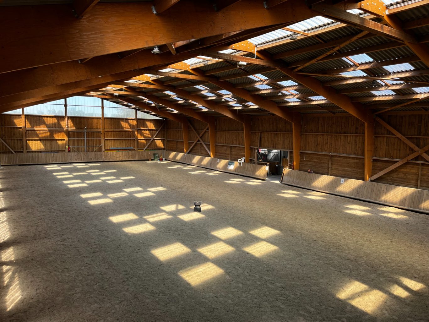 Manège de 20m x 40m Écurie spacieuse avec des rayons de soleil à travers les fenêtres et un sol sablonneux.