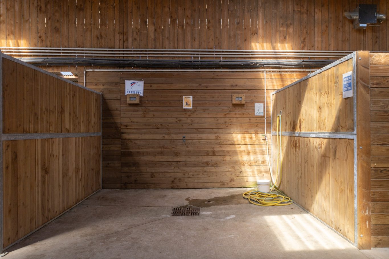 Douche avec eau chaude Écurie en bois avec des boxes vides et des panneaux d'affichage sur les murs.